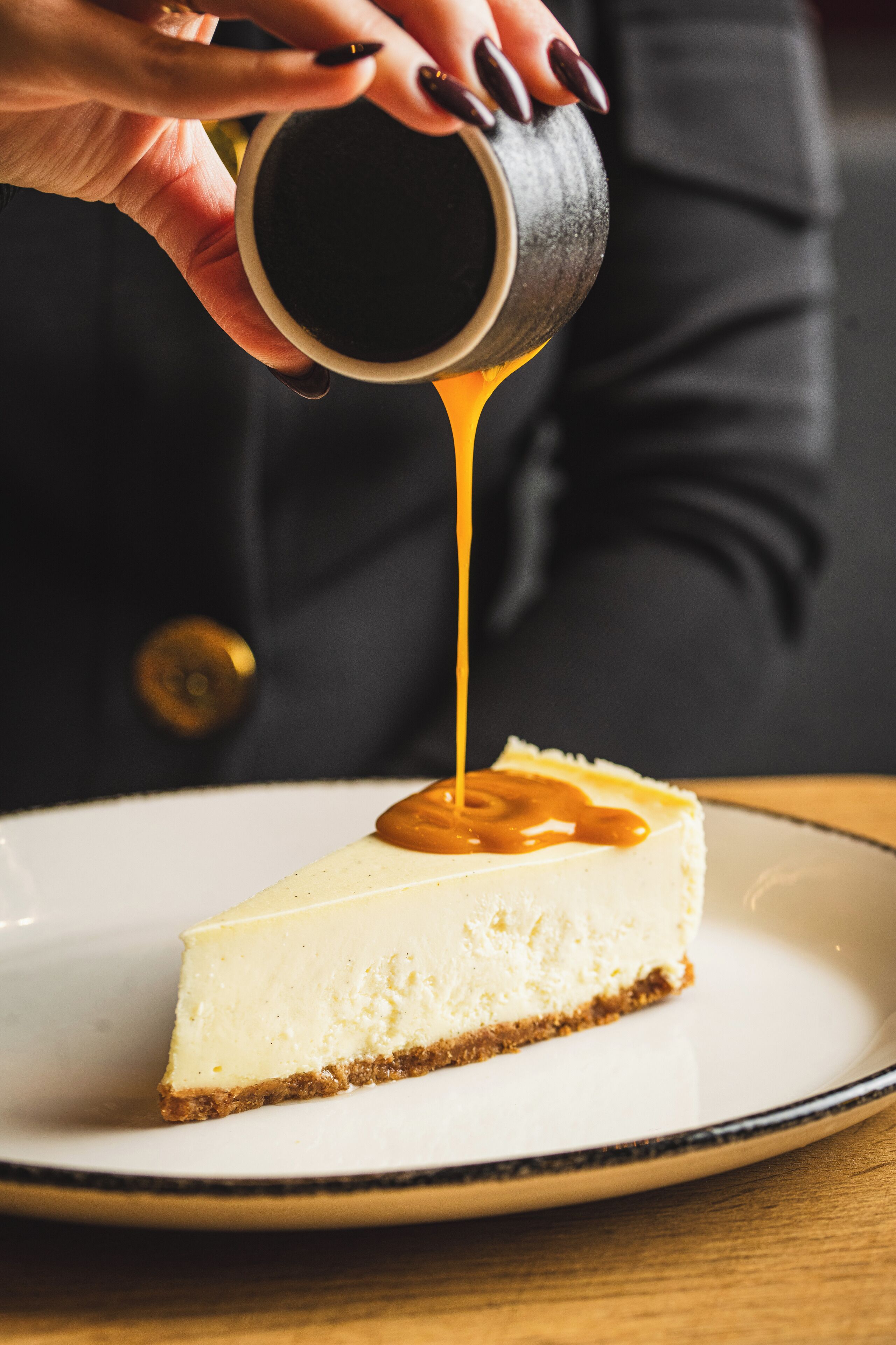 A slice of cheesecake with caramel sauce being poured over it.