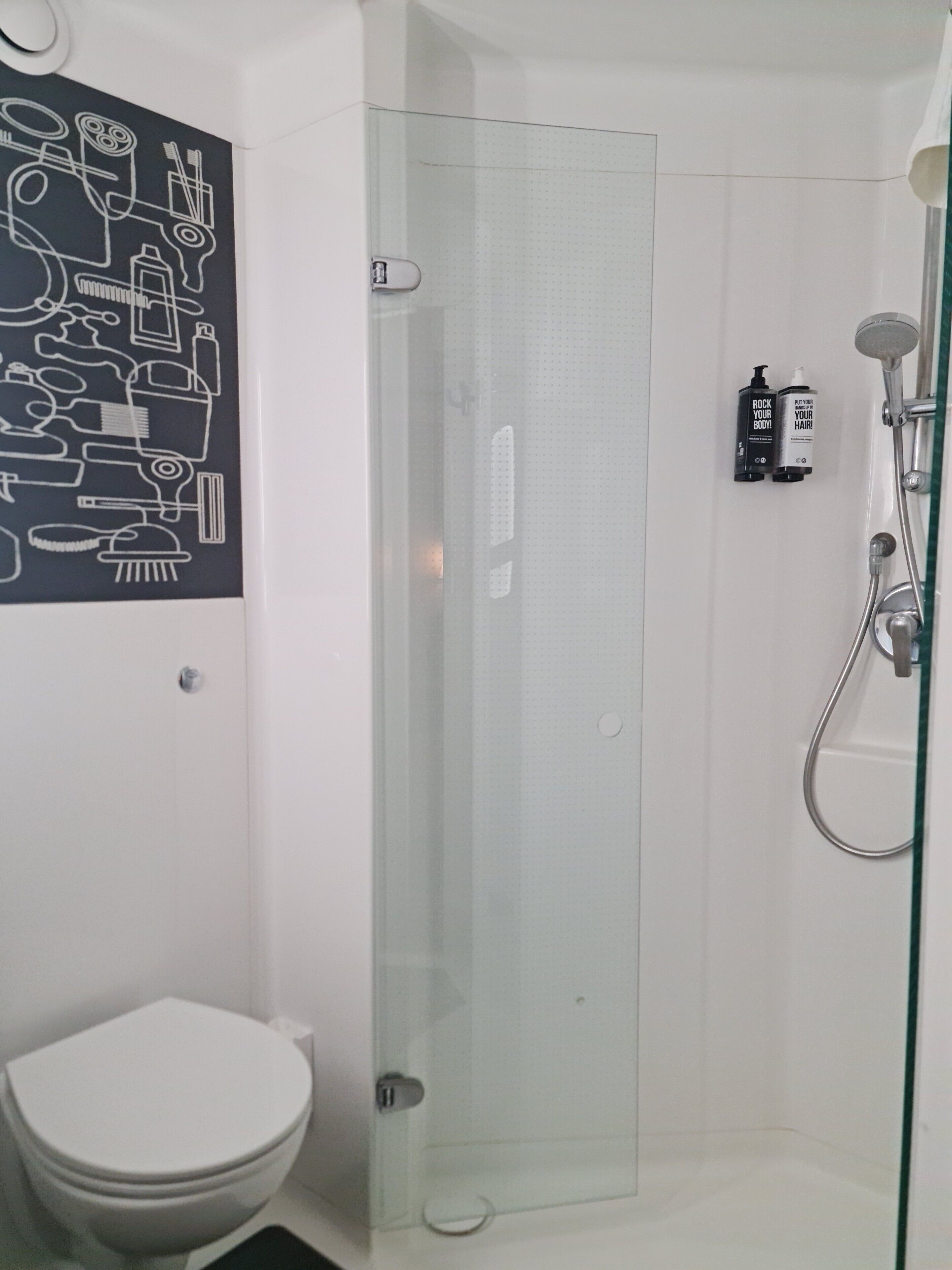 Ein Badezimmer mit Duschkabine aus Glas, Toilette und Wandseifenspender.