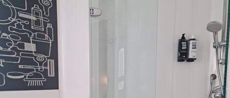 A bathroom with a glass shower enclosure, a toilet, and a wall-mounted soap dispenser.