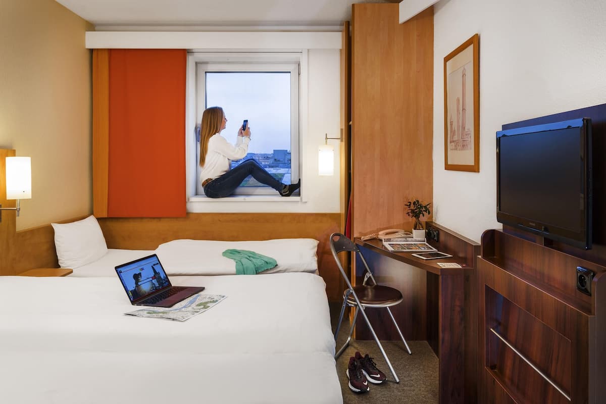 Une chambre d’hôtel avec un lit, un bureau avec un ordinateur portable, une chaise, une télévision et une fenêtre donnant sur un paysage agréable.