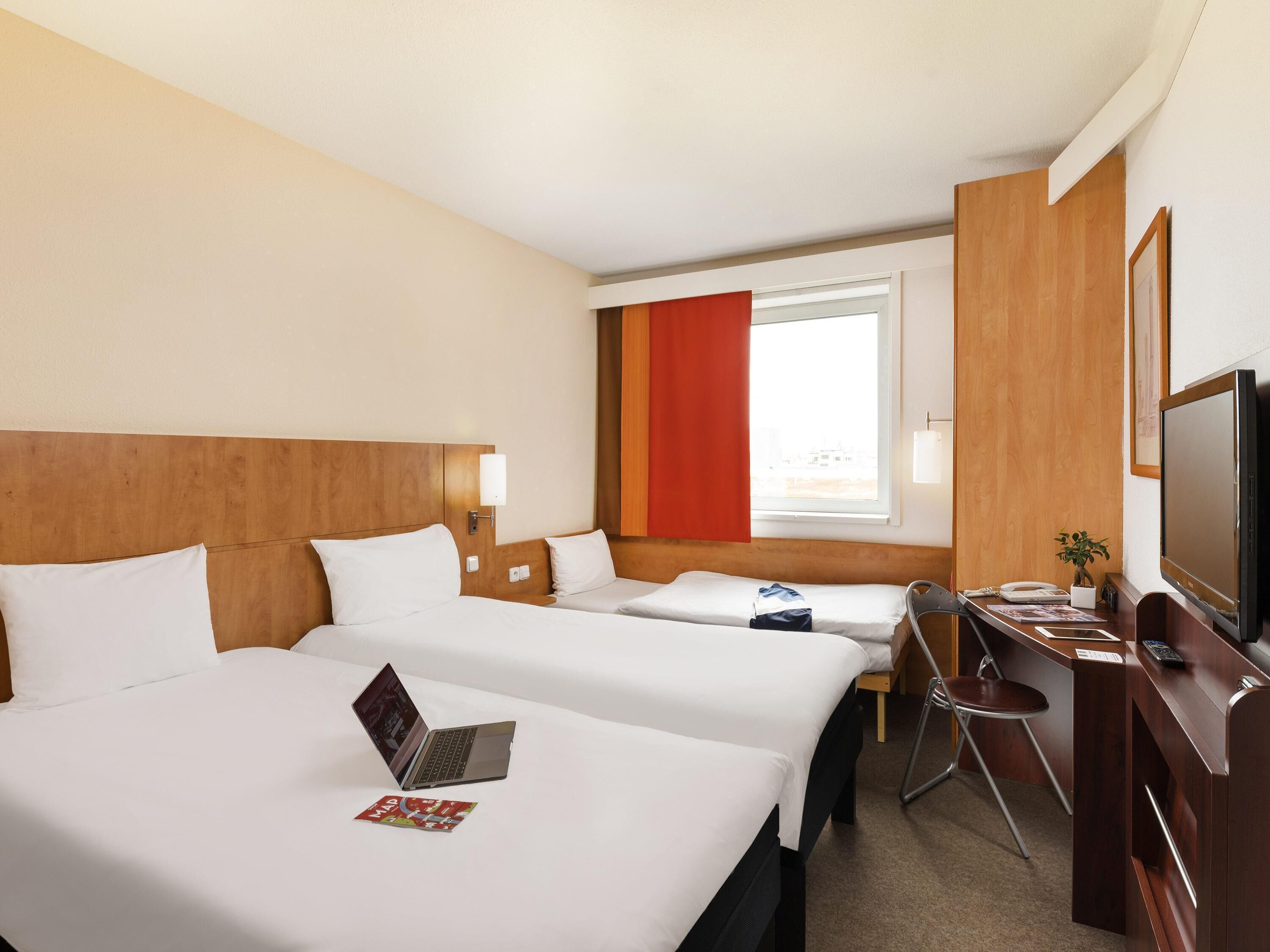 Habitación de hotel con dos camas, un escritorio, un televisor y una ventana.