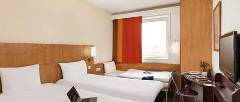 A hotel room with two beds, a desk, a TV, and a window.