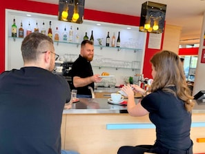 A bar area with a counter, shelves with bottles, and a coffee machine. - ibis Praha Mala Strana (Prague)