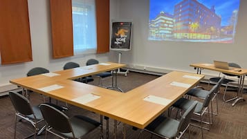 Un salón de conferencias con una larga mesa, sillas, una pantalla de proyector y un cartel en la pared.