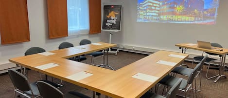 Un salón de conferencias con una larga mesa, sillas, una pantalla de proyector y un cartel en la pared.
