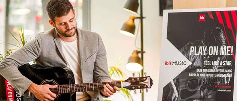 Una persona tocando la guitarra en una habitación con un cartel publicitario de un servicio de música.