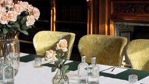 A dining table set with a vase of flowers, salt and pepper shakers, and a candle. There are chairs around the table, and a fireplace is visible in the background.