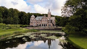A large, historic building with a symmetrical facade, surrounded by lush greenery and a calm water body with lily pads. - Landgoed Duin & Kruidberg (Santpoort-Noord)
