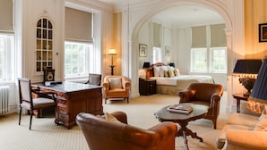 A spacious room with a large desk, comfortable seating, a bed, and a chandelier.