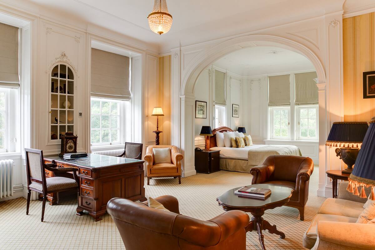 A spacious room with a large desk, comfortable seating, a bed, and a chandelier.