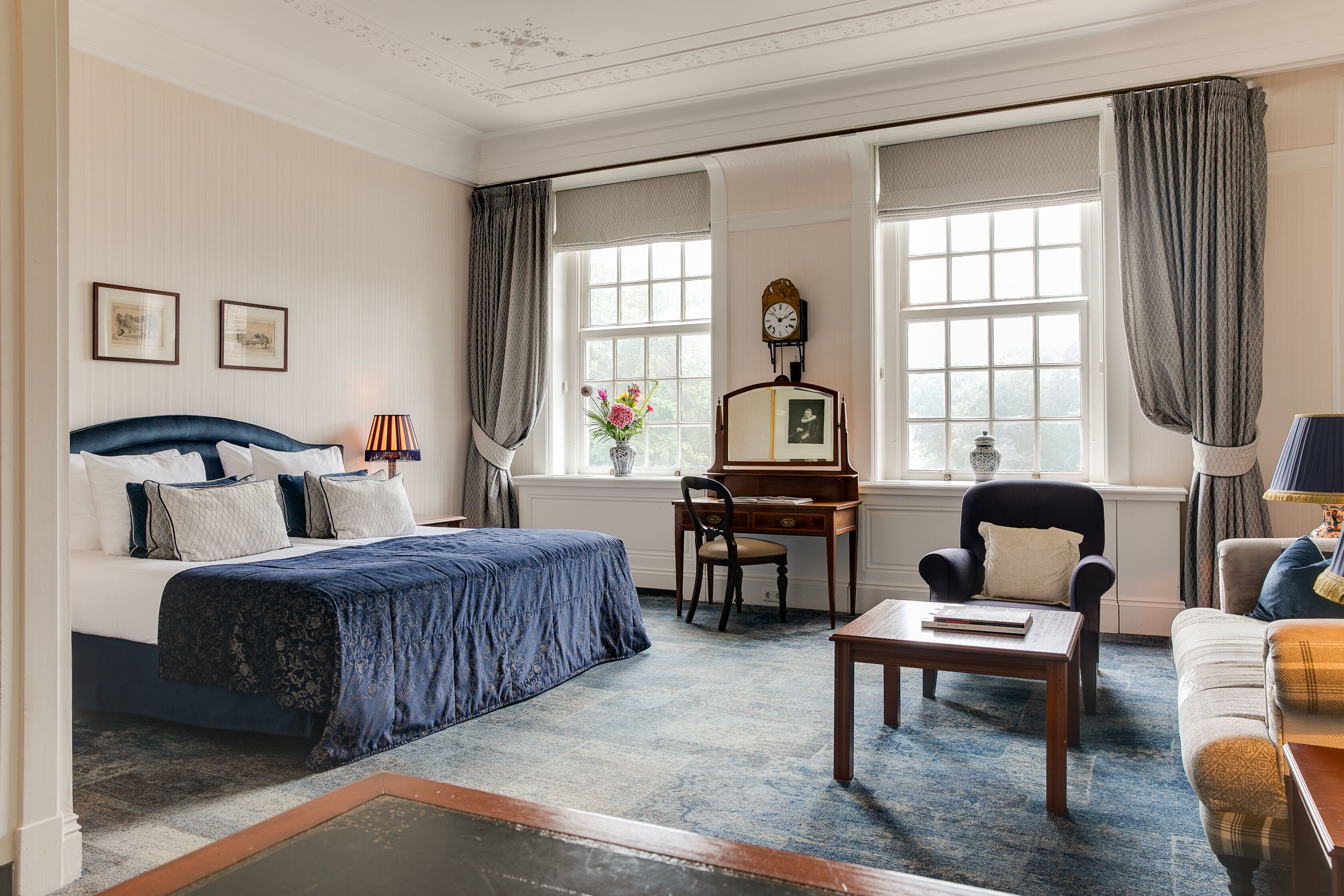A bedroom with a bed, a desk, a chair, a coffee table, and a window with curtains.