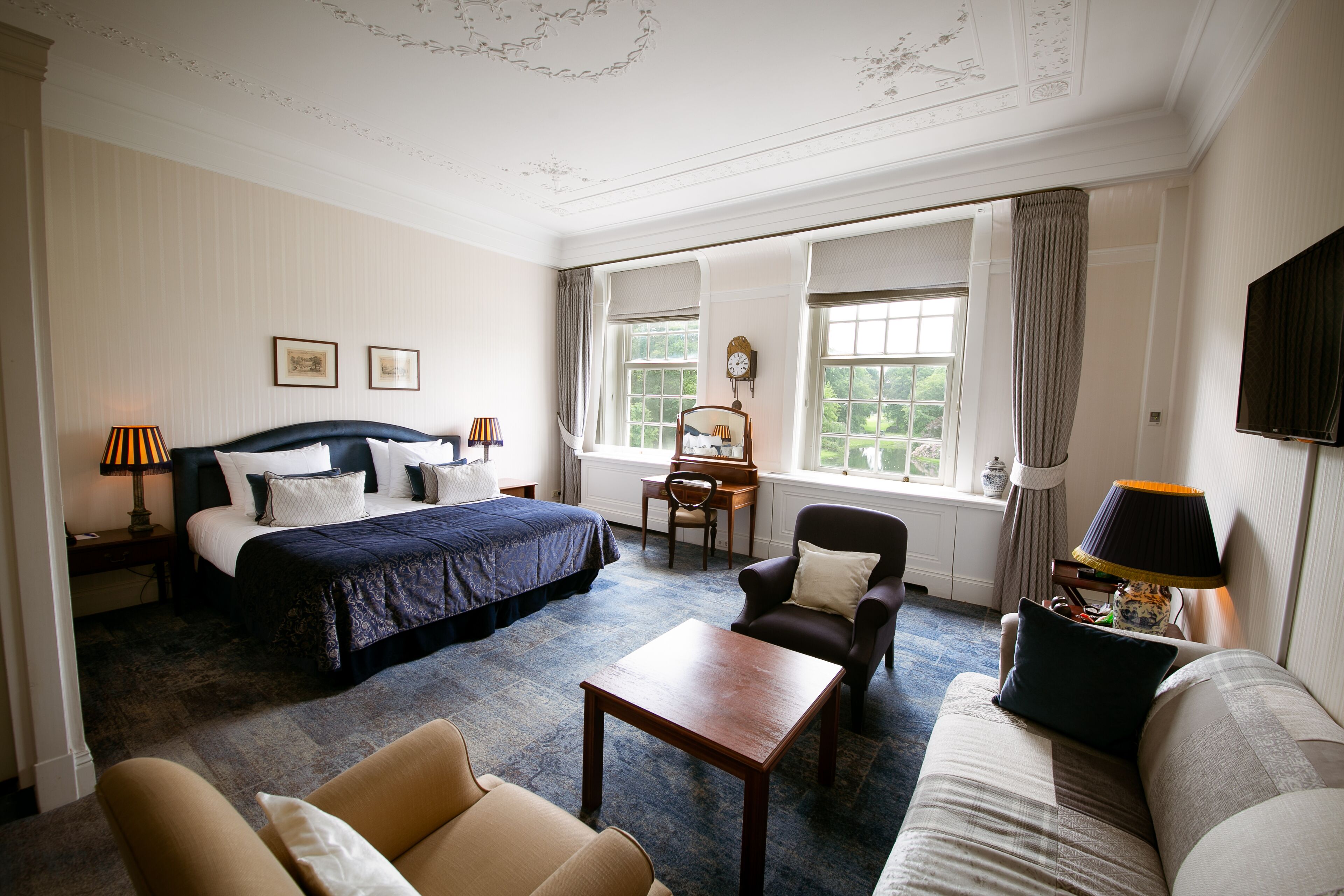 A hotel room with a large bed, a sitting area with a sofa and armchairs, a small table, and a desk with a chair.