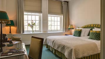 Una habitación de hotel con una cama grande, dos mesitas de noche, una silla, un escritorio y una ventana con cortinas.