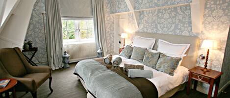 A bedroom with a large bed, two bedside tables, a chair, and a window with curtains.