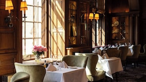A dining area with tables set for service, large windows with natural light, and classic wooden paneling.