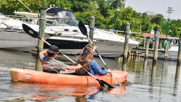 Two people in a canoe on calm water with boats docked in the background.