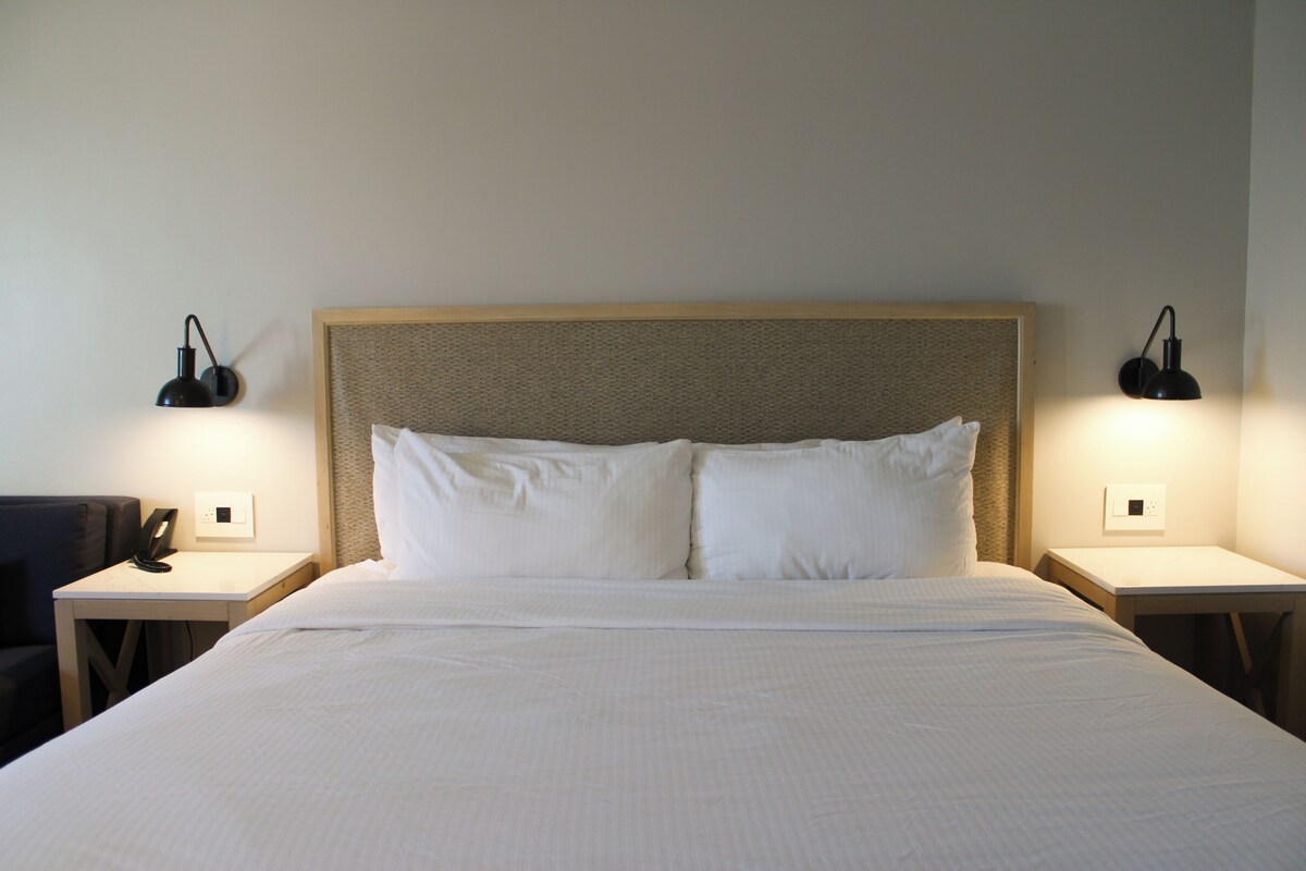 A neatly made bed with white linens, two bedside tables with lamps, and a wall-mounted light fixture.