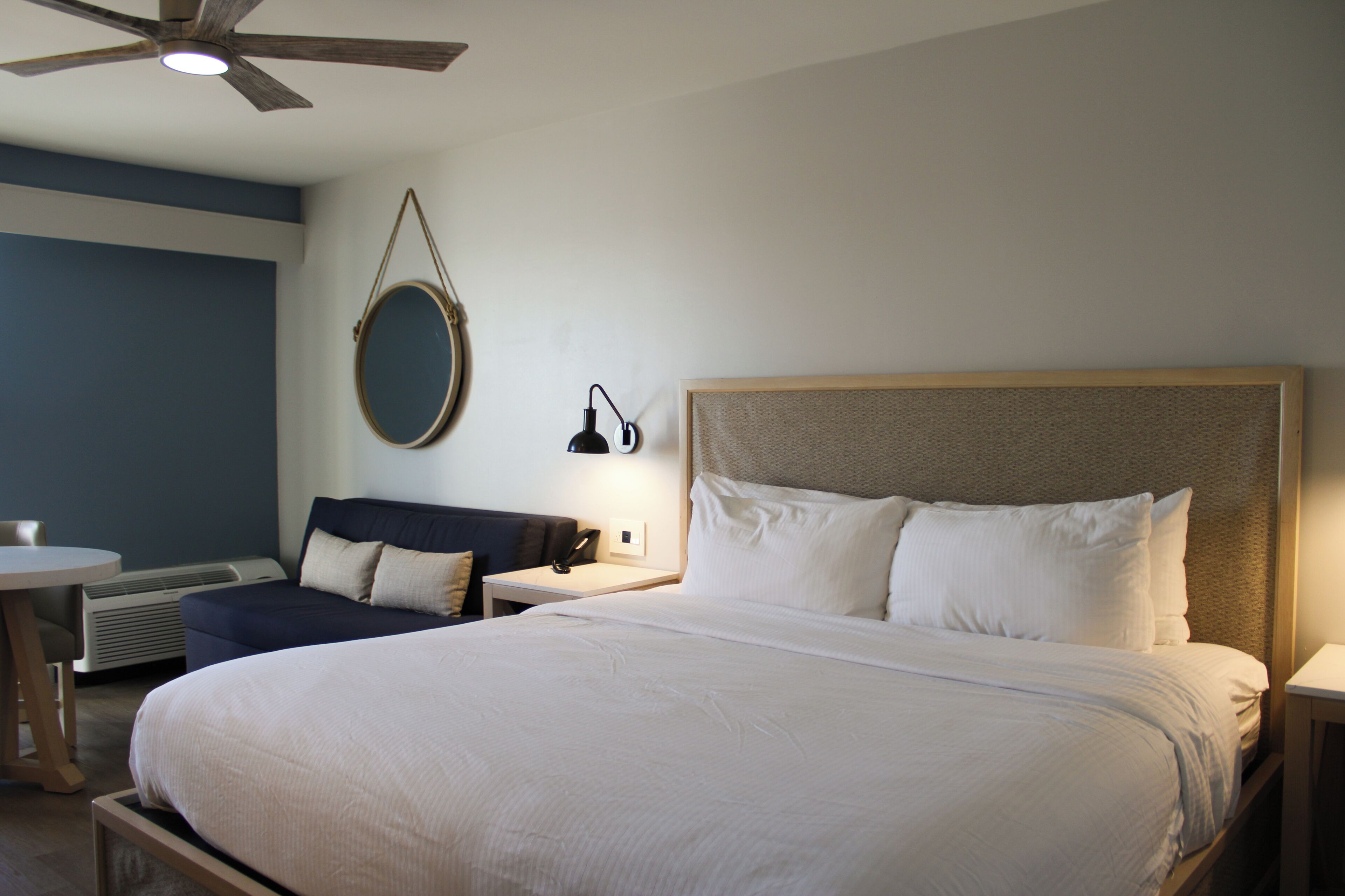 A hotel room with a large bed, bedside tables, a round mirror, and a ceiling fan.