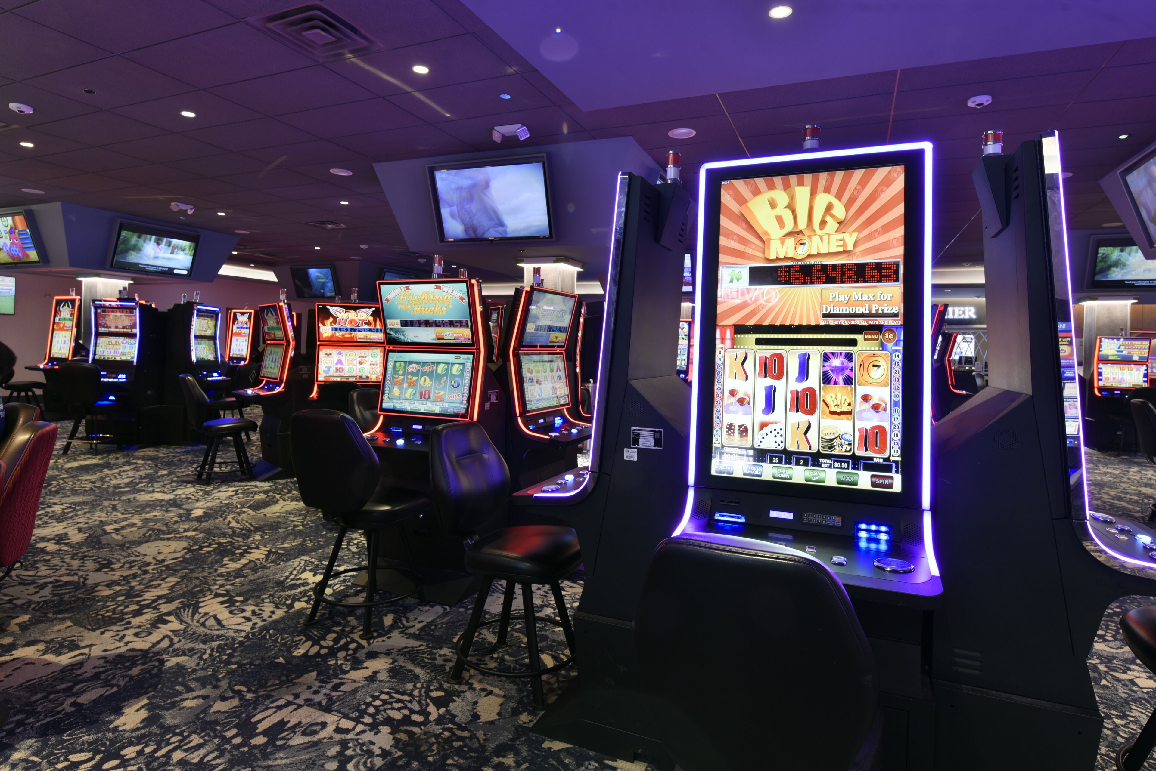 Un casino con varias máquinas tragamonedas y una pantalla grande mostrando 'BIA MONEY'.