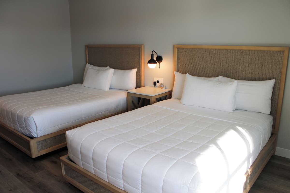 Two adjacent beds with wooden headboards, a bedside table with a lamp, and a wall clock.
