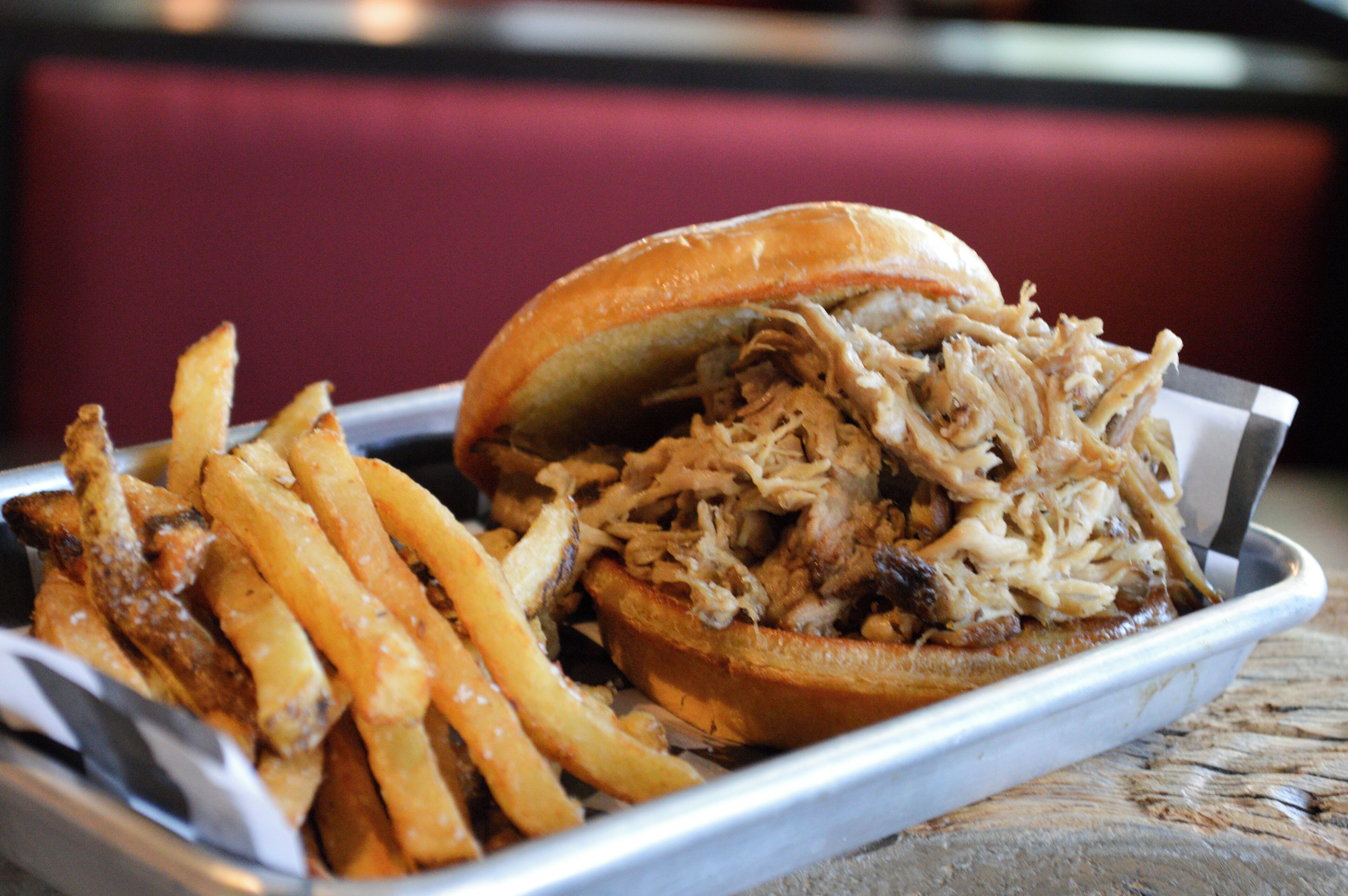 A pulled pork sandwich with fries on a tray.