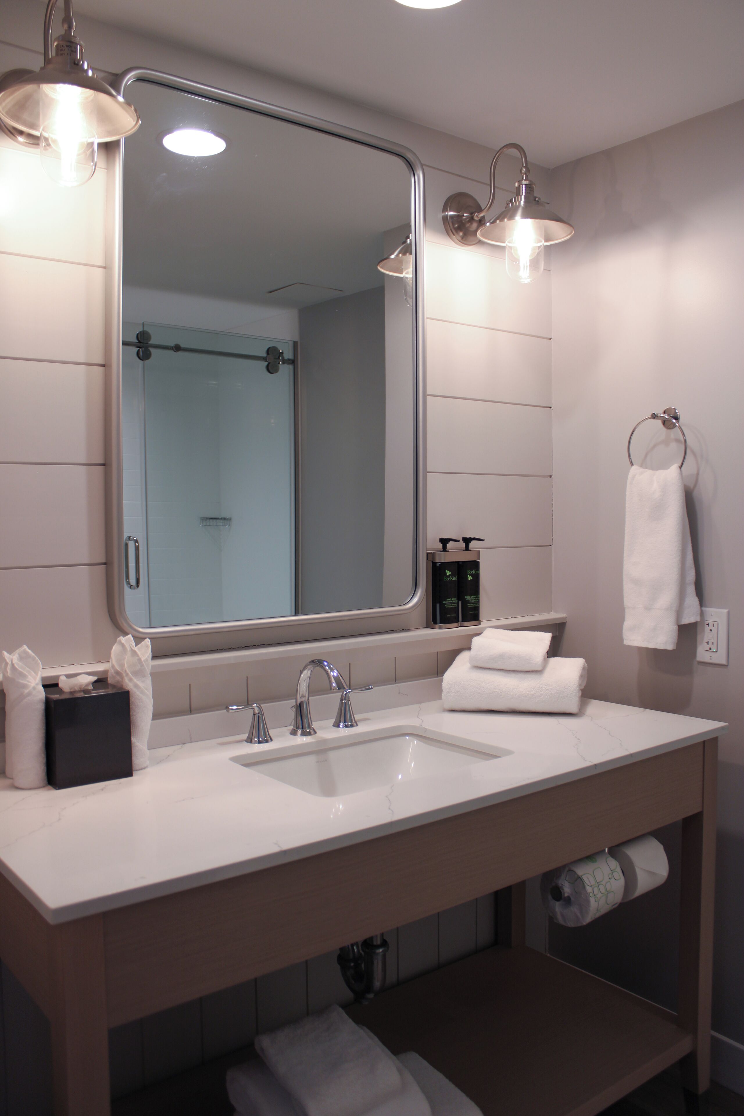 A bathroom with a large mirror, two sinks, and a towel rack.