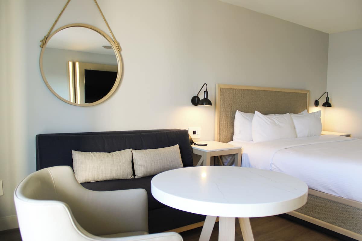 A hotel room with a bed, a sofa, a round table, and a hanging mirror.