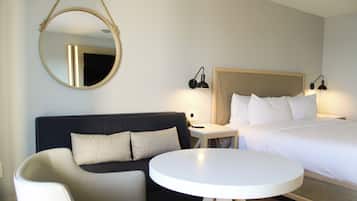 A hotel room with a bed, a sofa, a round table, and a hanging mirror.