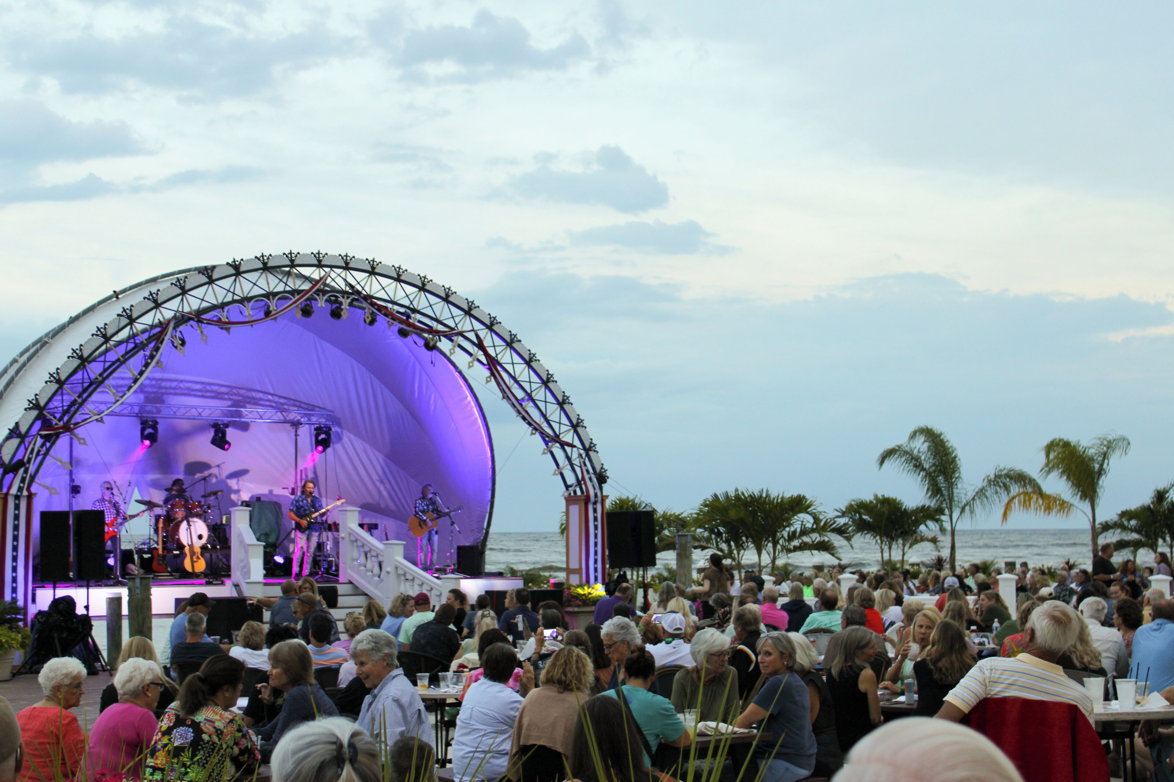 A stage with musicians performing, surrounded by seated guests at an outdoor event.