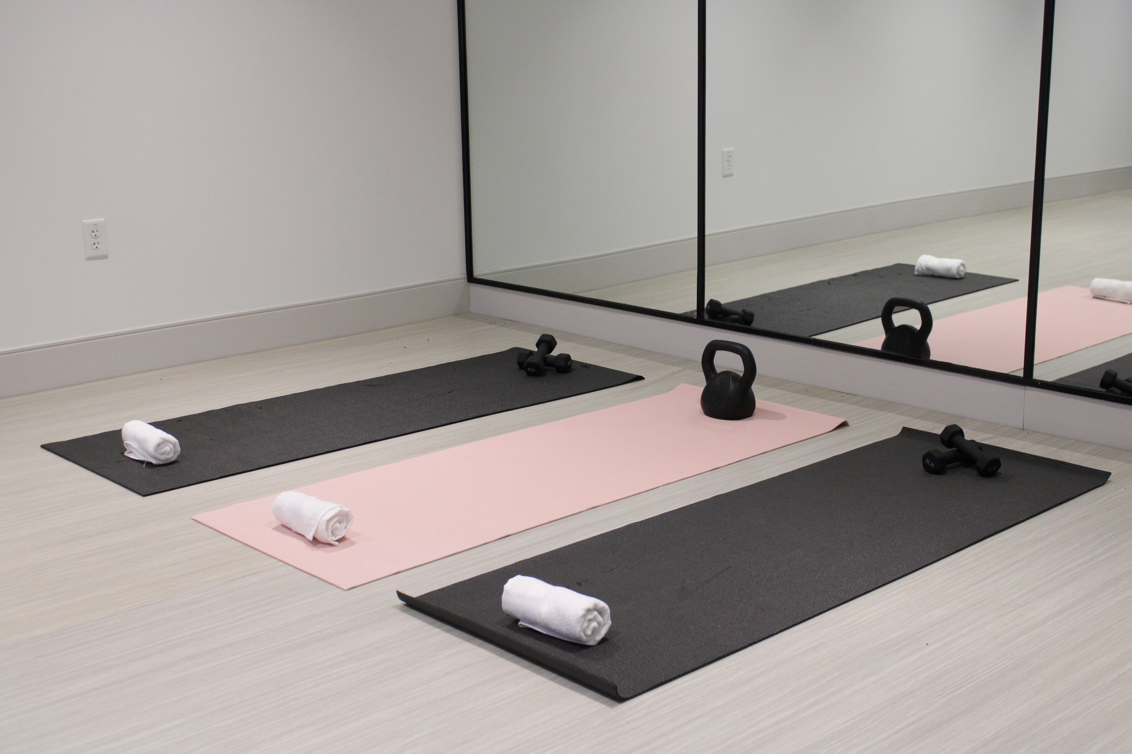 A gym with black and pink mats, kettlebells, and rolled-up towels.