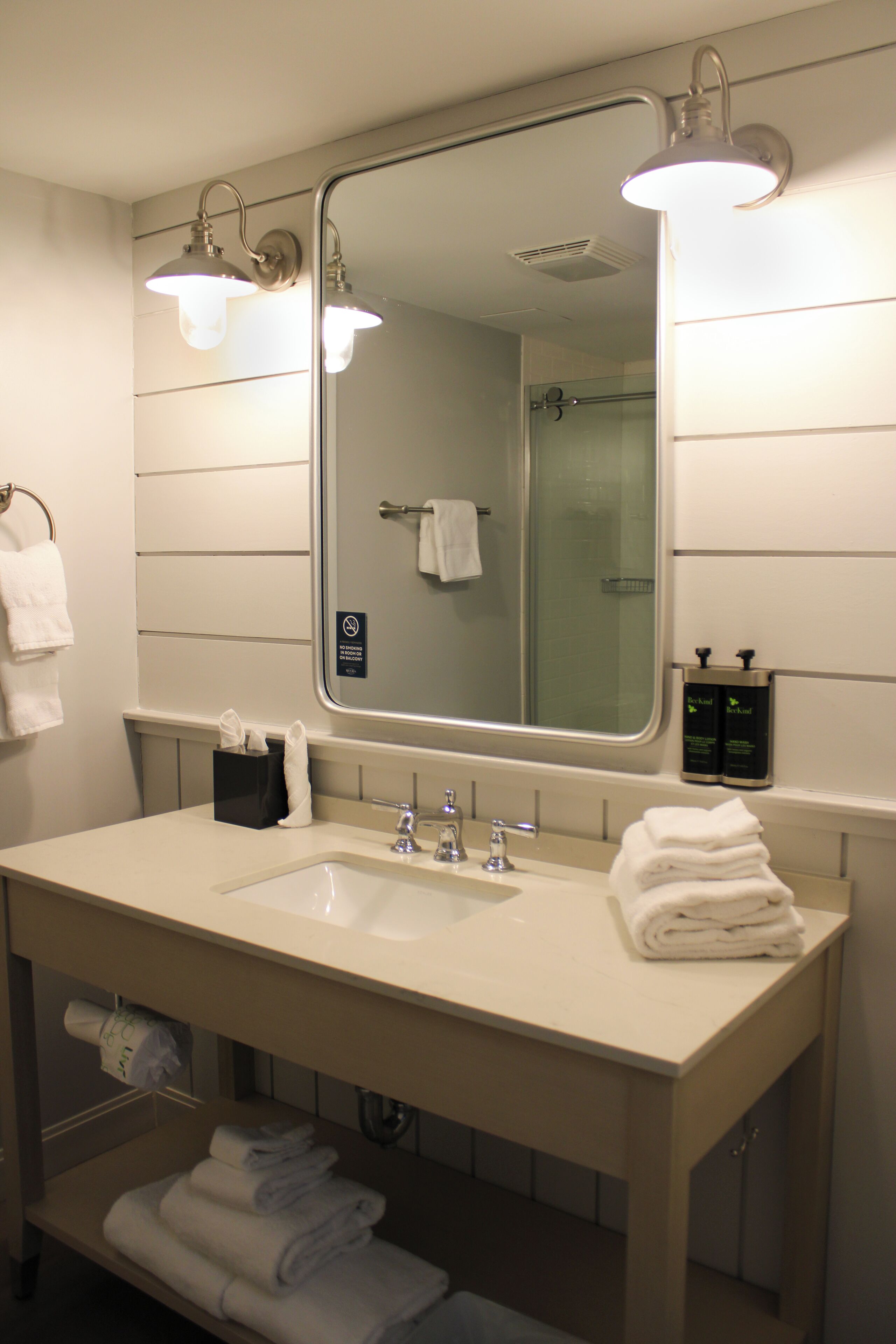 A hotel bathroom with a large mirror, two sinks, and a towel rack.