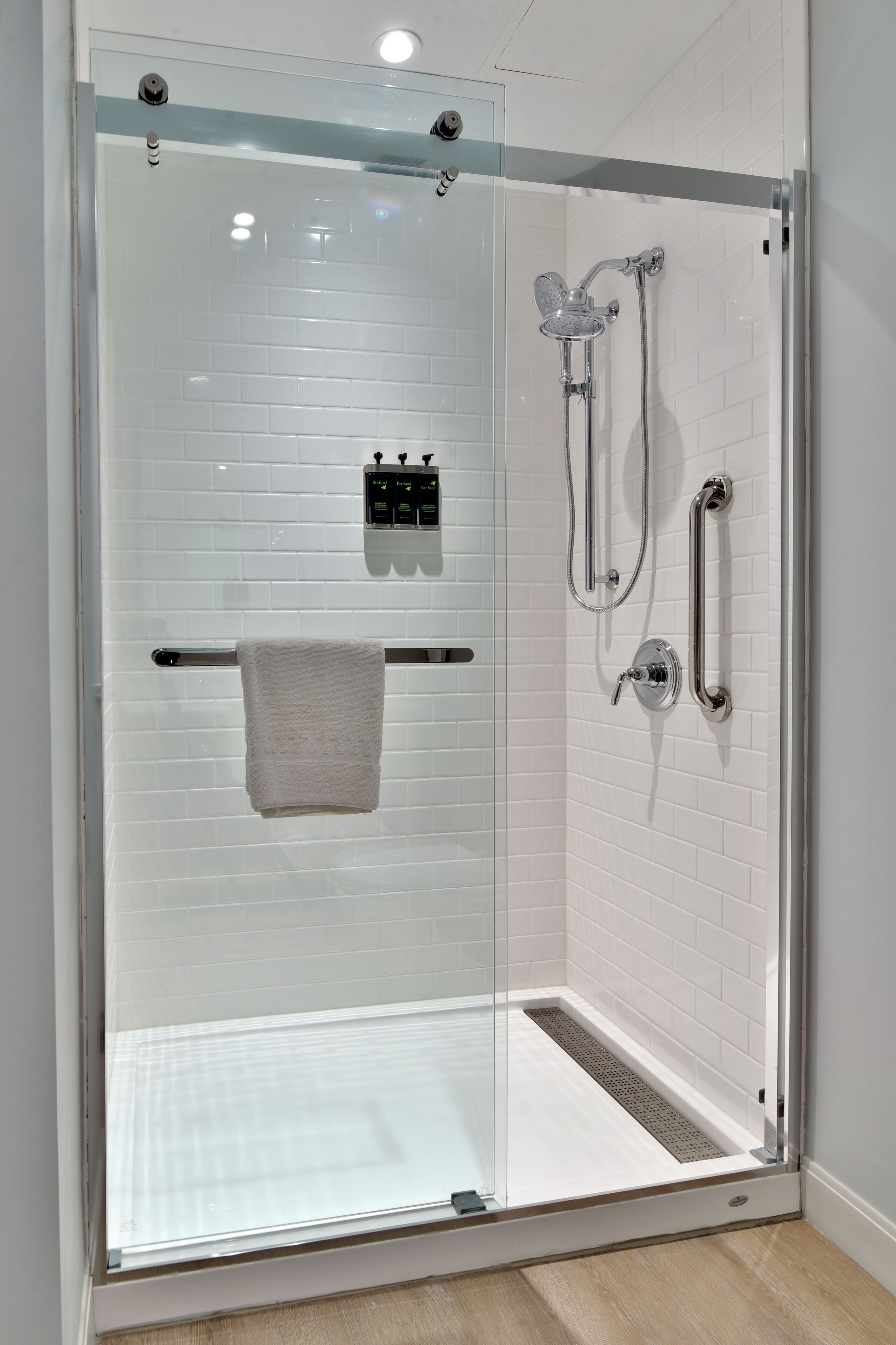 Une douche fermée par des parois de verre, avec un mur recouvert de carreaux blancs, un porte-serviettes et une douchette à main.