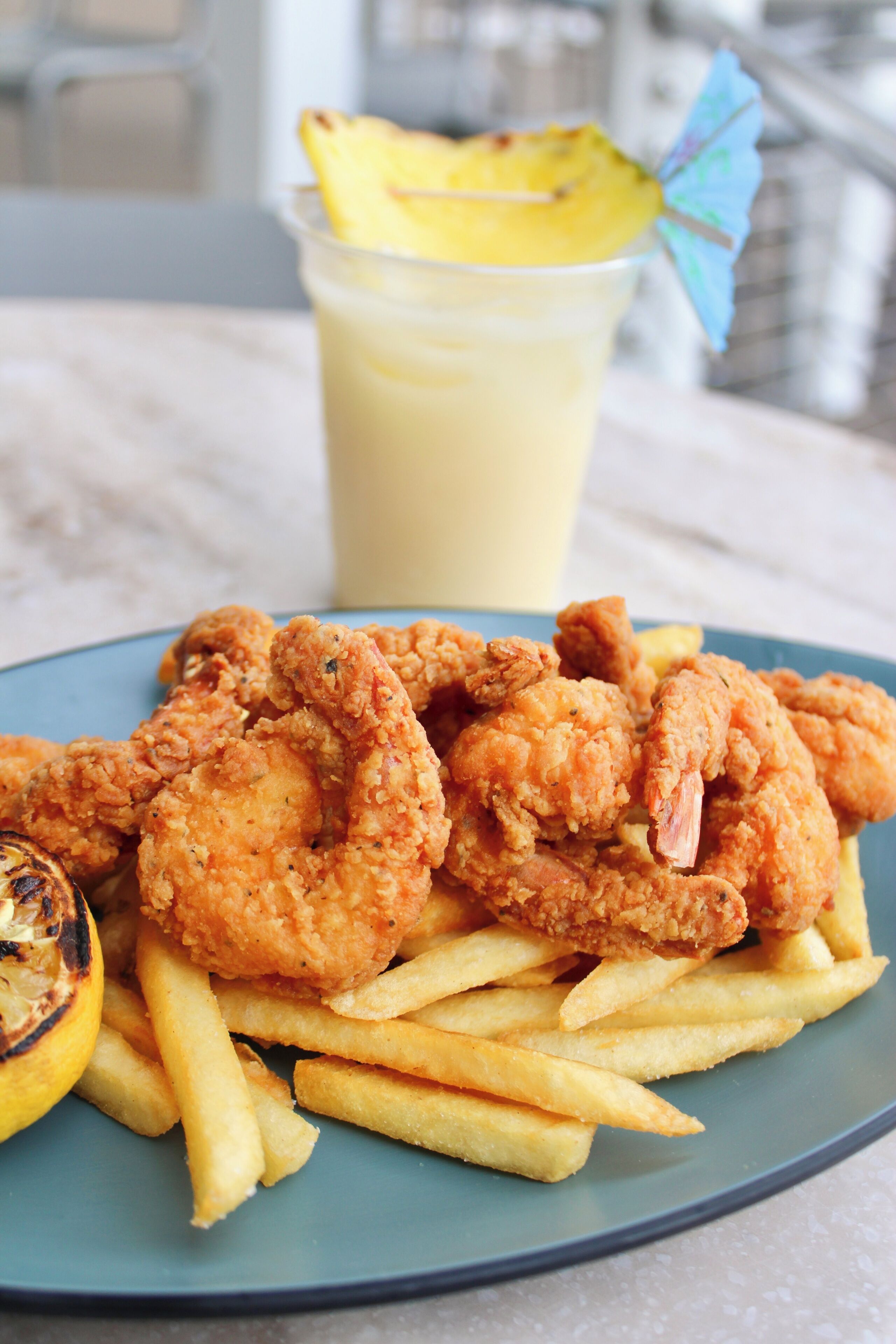 Une assiette de crevettes frites et de frites, avec une boisson en arrière-plan.