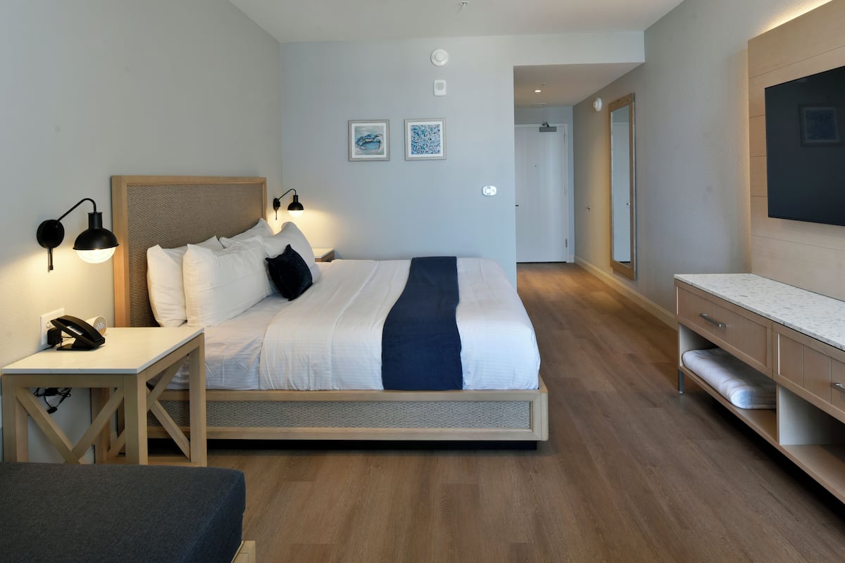 A modern hotel room with a bed, bedside table, lamp, and a flat-screen TV.