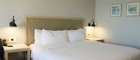 A neatly made bed with white linens, two bedside lamps, and two framed artworks on the wall.
