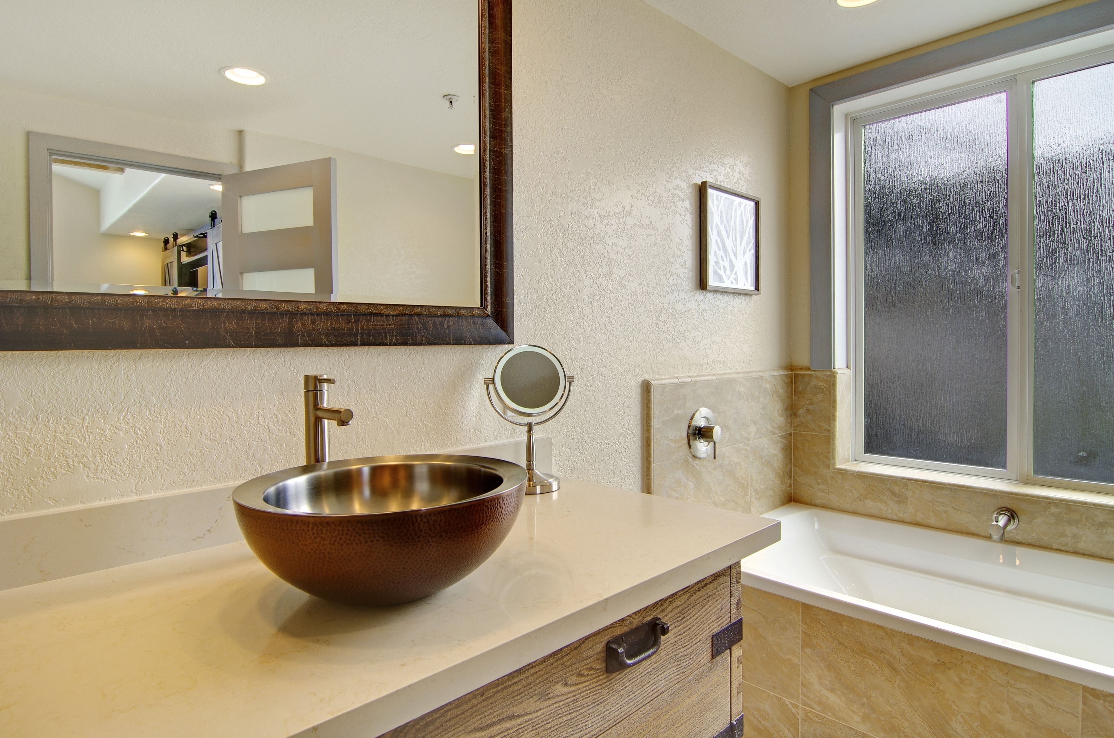 A bathroom with a large mirror, a round mirror, a vessel sink, and a bathtub.