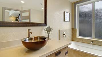 A bathroom with a large mirror, a round mirror, a vessel sink, and a bathtub.