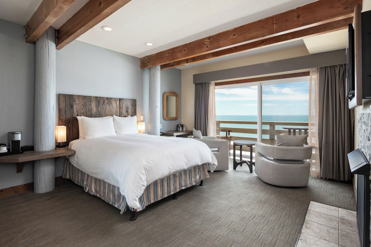 A hotel room with a large bed, a seating area with a view of the sea, and a balcony.