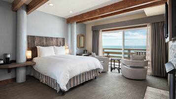 Habitación de hotel con una cama grande, zona de estar con vista al mar y un balcón.