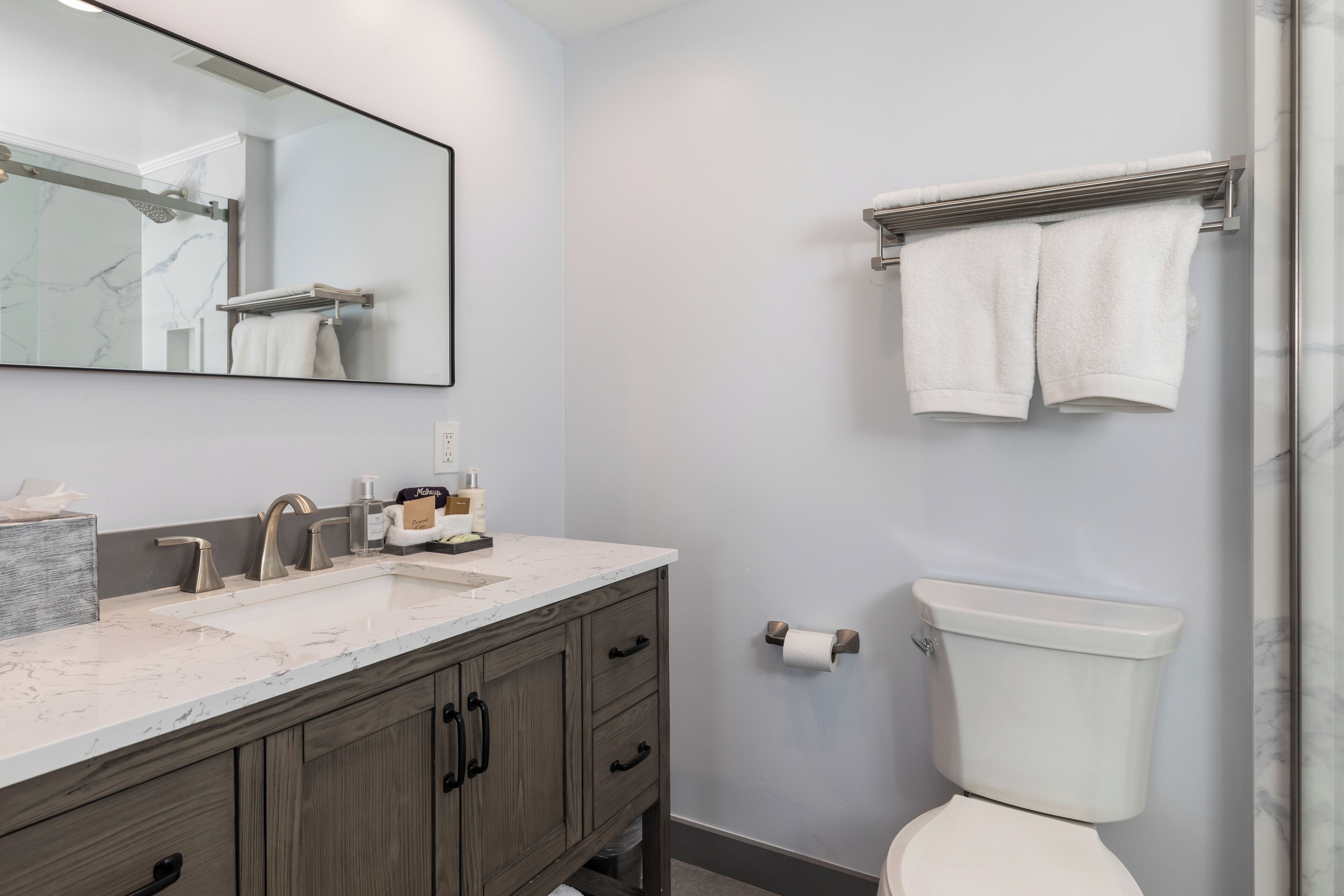 A bathroom with a marble sink, wooden cabinets, a toilet, and a towel rack.