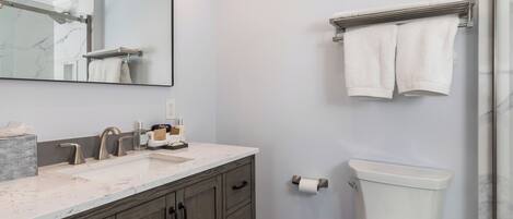 A bathroom with a marble sink, wooden cabinets, a toilet, and a towel rack.