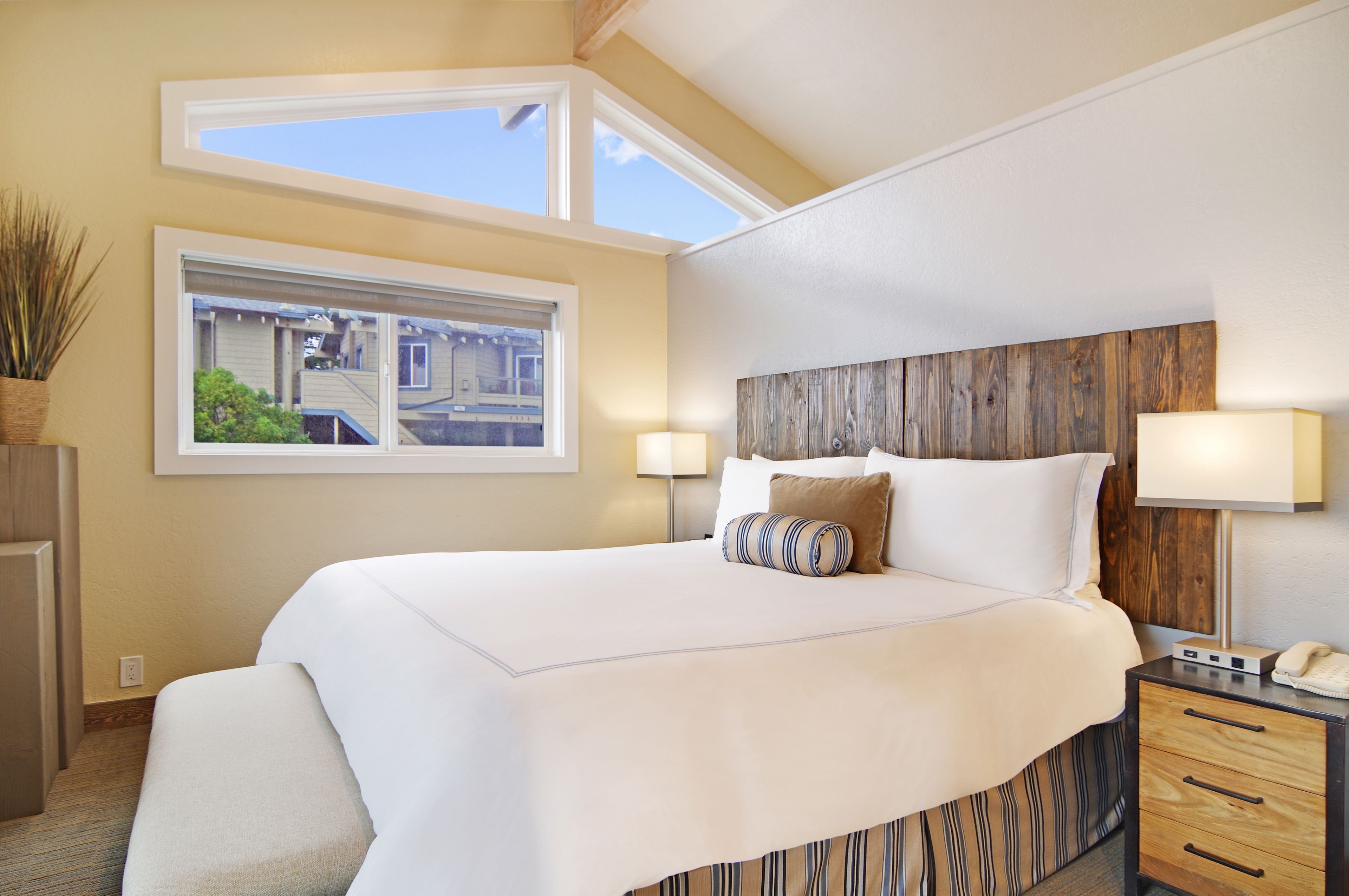 A neatly made bed with a wooden headboard, two bedside lamps, and a window with a view of buildings.
