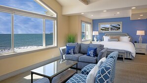 Un dormitorio con un ventanal grande que da al mar, una cama con ropa de cama azul, un sofá con cojines azules y una mesita de noche.