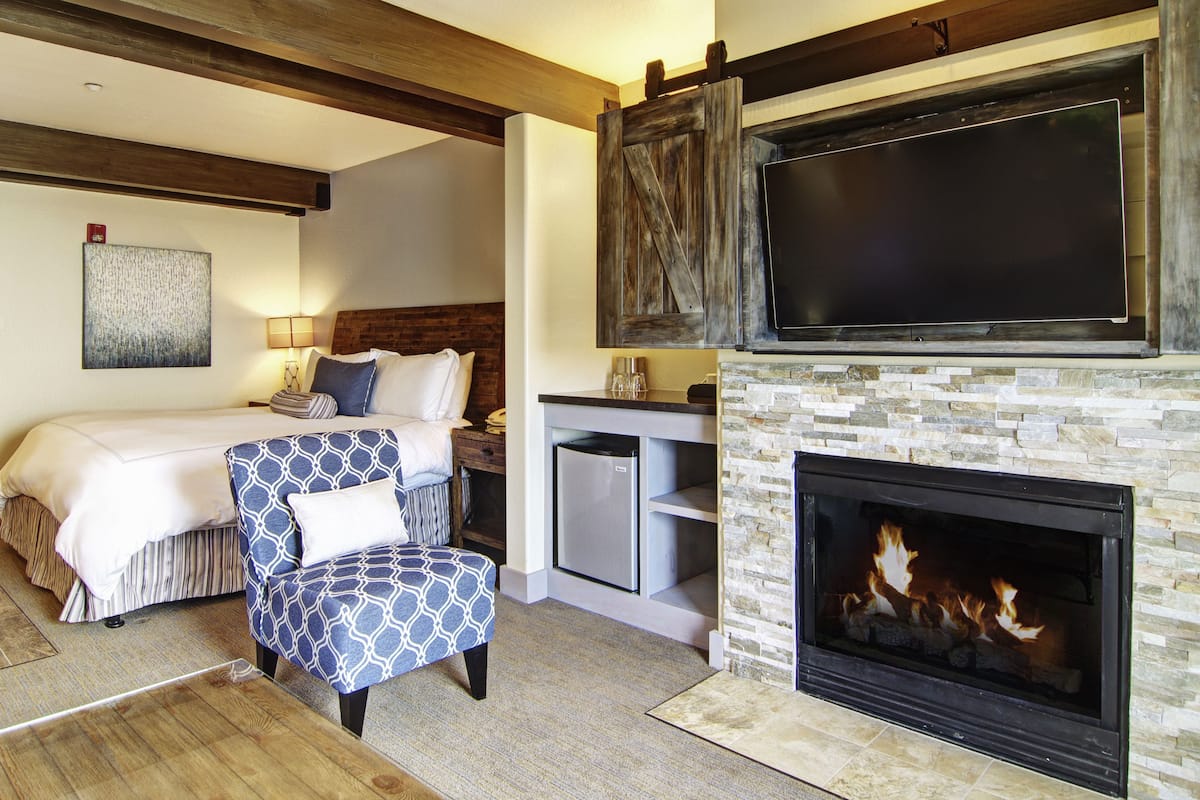A hotel room with a bed, a chair, a TV, a fireplace, and a stone wall.