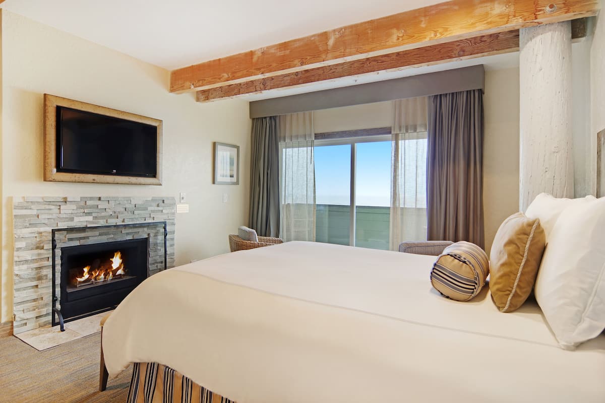 A hotel room with a stone fireplace, a bed with pillows, a flat-screen TV, and a large window with curtains.
