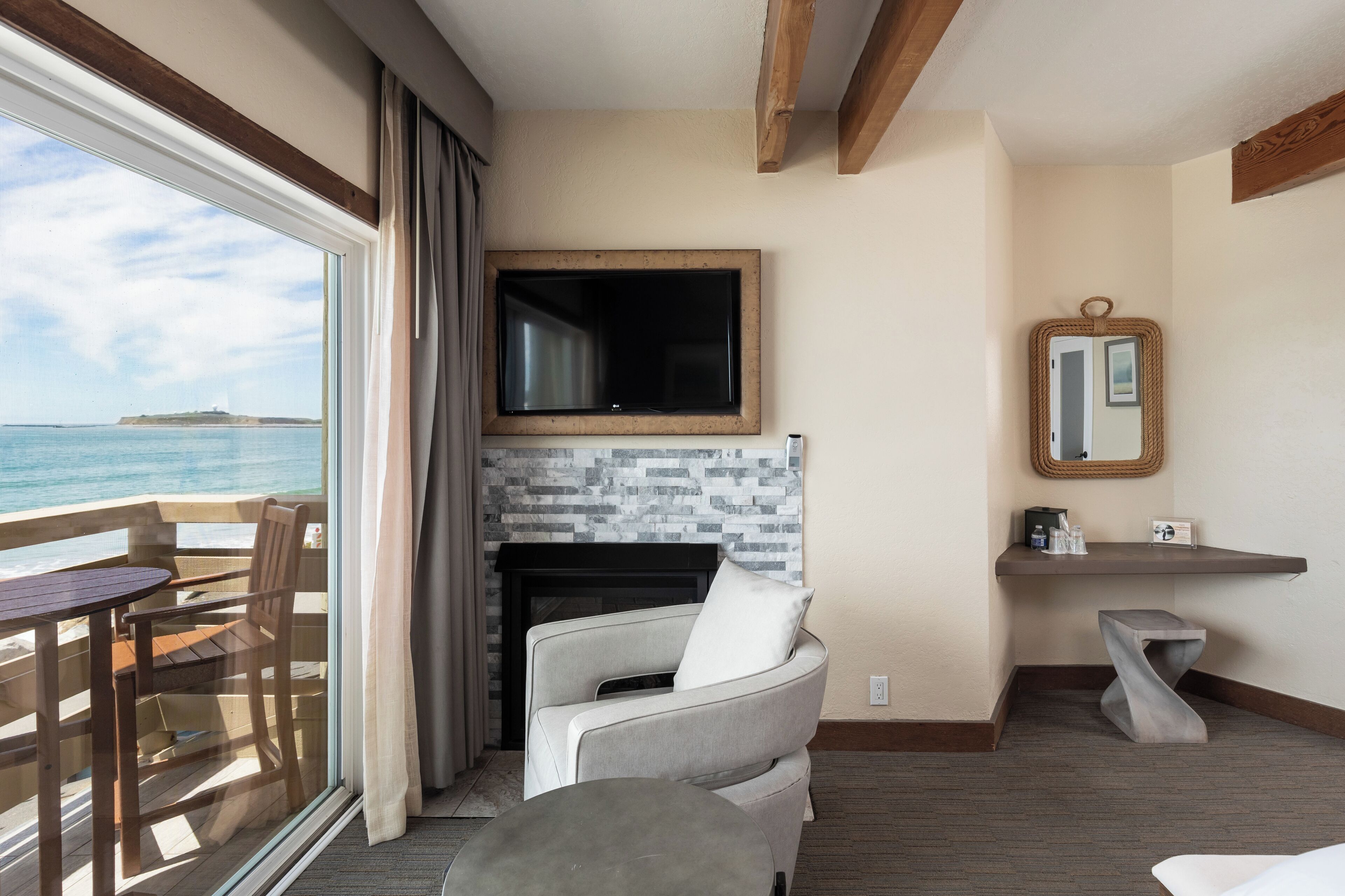 A room with a view of the sea, a fireplace, a television, and a small table.