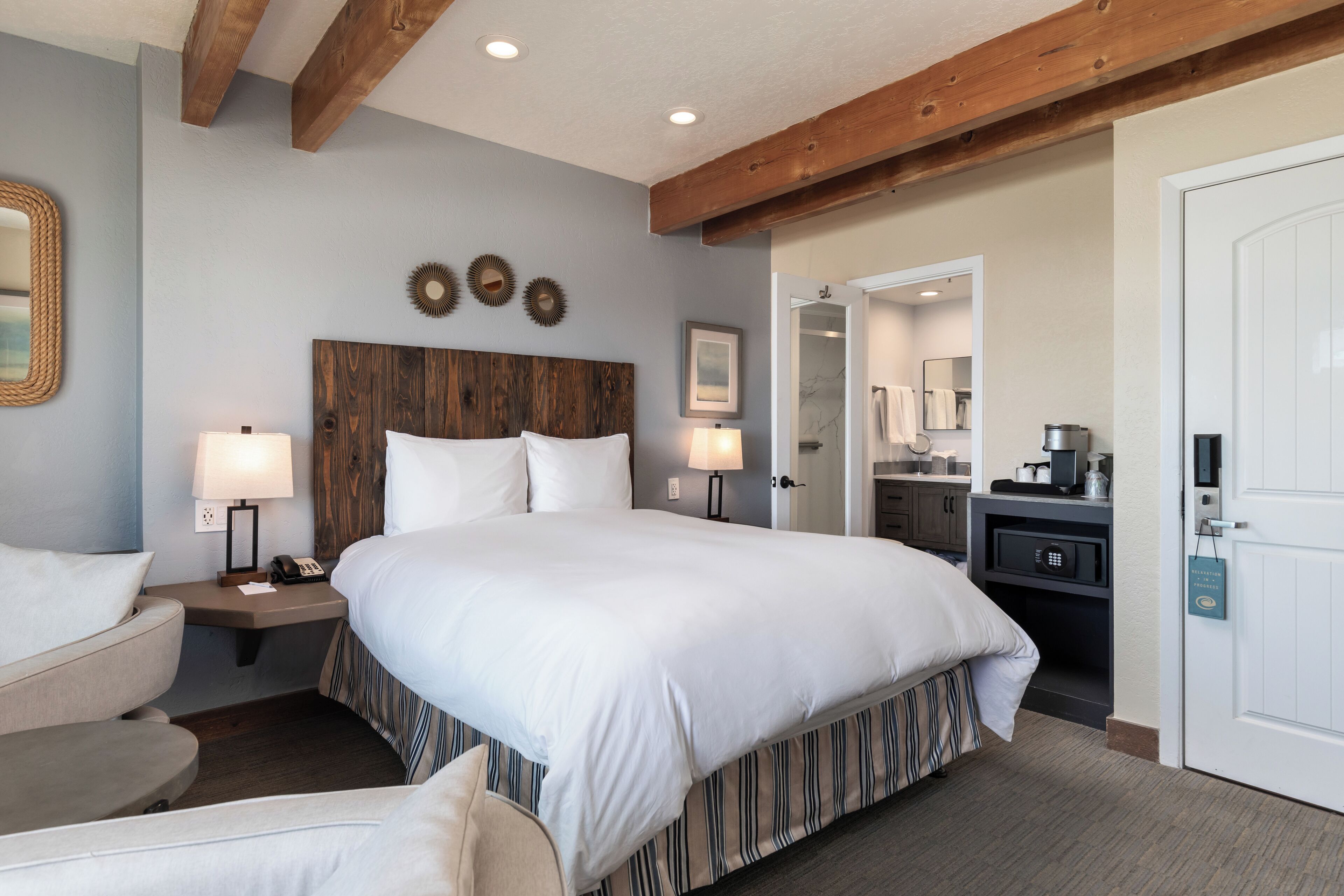Une chambre d’hôtel avec un grand lit, une tête de lit en bois, deux tables de chevet avec des lampes, un petit bureau avec une chaise et une armoire.