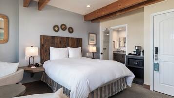 Une chambre d’hôtel avec un grand lit, une tête de lit en bois, deux tables de chevet avec des lampes, un petit bureau avec une chaise et une armoire.