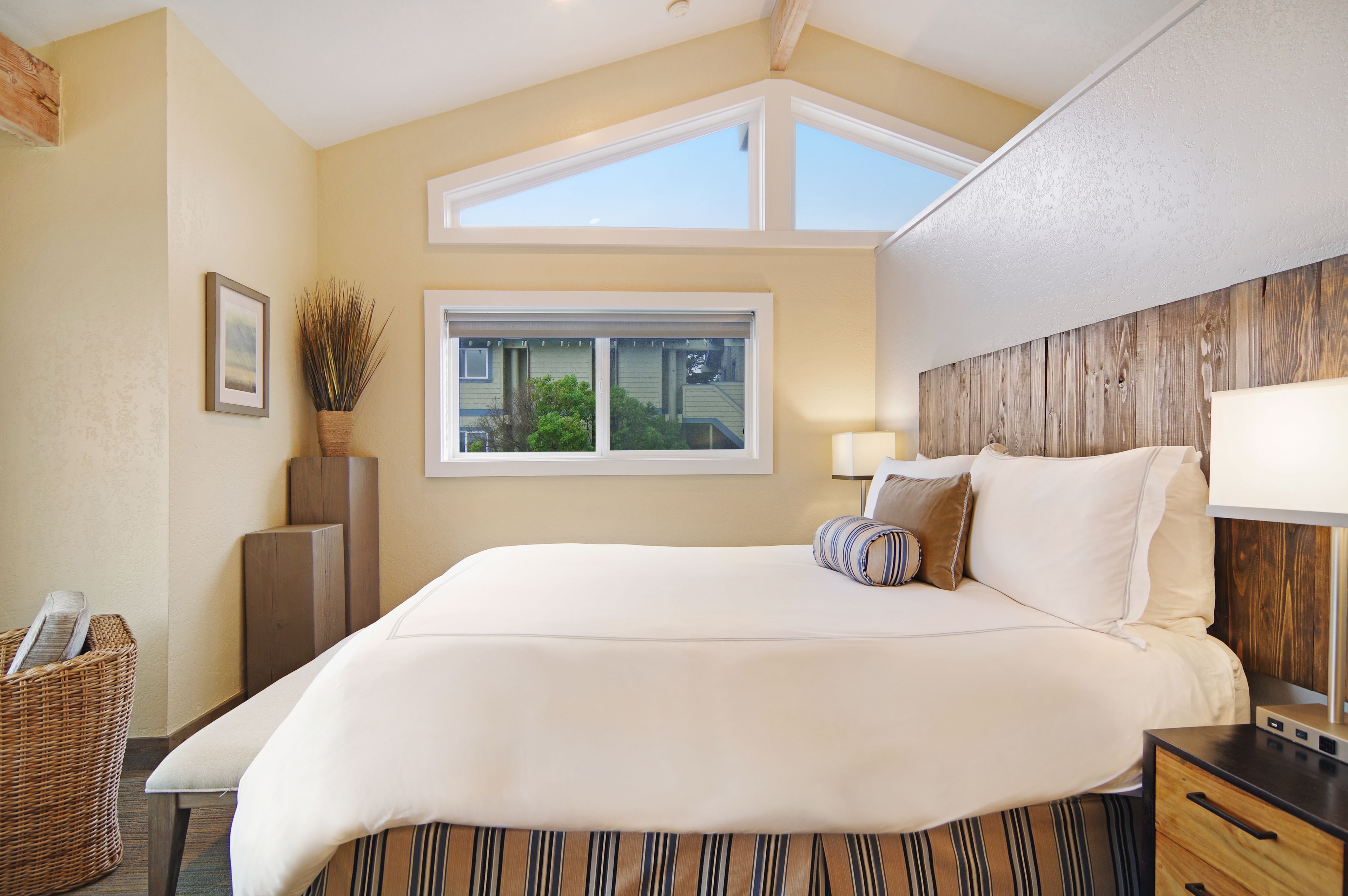 A bedroom with a large bed, a window, a nightstand, and a lamp.