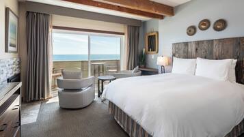 A hotel room with a large bed, a desk, a chair, and a view of the ocean.